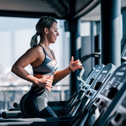 Side view of beautiful muscular woman running on treadmill.